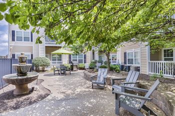 A patio with a fountain and chairs is surrounded by trees.